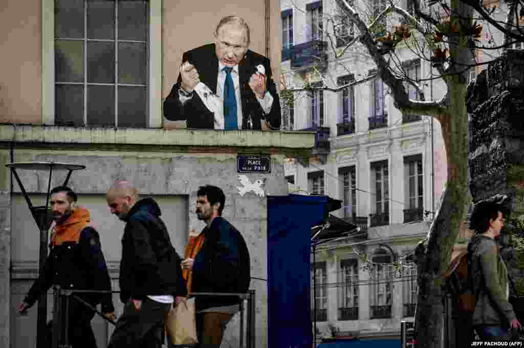 Луѓе минуваат покрај мурал на кој е прикажан Путин како кине глава на гулаб, на Place de la Paix во Лион, Франција, на 22 март од непознат уметник.