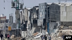 Refugiați palestinieni trec pe lângă dărâmăturile clădirilor din tabăra Maghazi, grav avariată de bombardamentele israeliene.