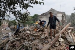 Localnici din Ciuhuiv caută documente ale prietenului lor rănit, printre resturile unei case distruse de bombardamentele rusești, regiunea Harkov, Ucraina, 16 iulie 2022.