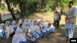 A Security official stands guard as school girls attend their school in open air following the school building destruction by suspected militants, in Tirah valley, in Khyber tribal district. (file photo)