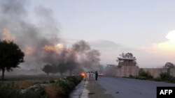 FILE: Afghan men watch the aftermath of a suicide car bomb attack on a military base in Khost.