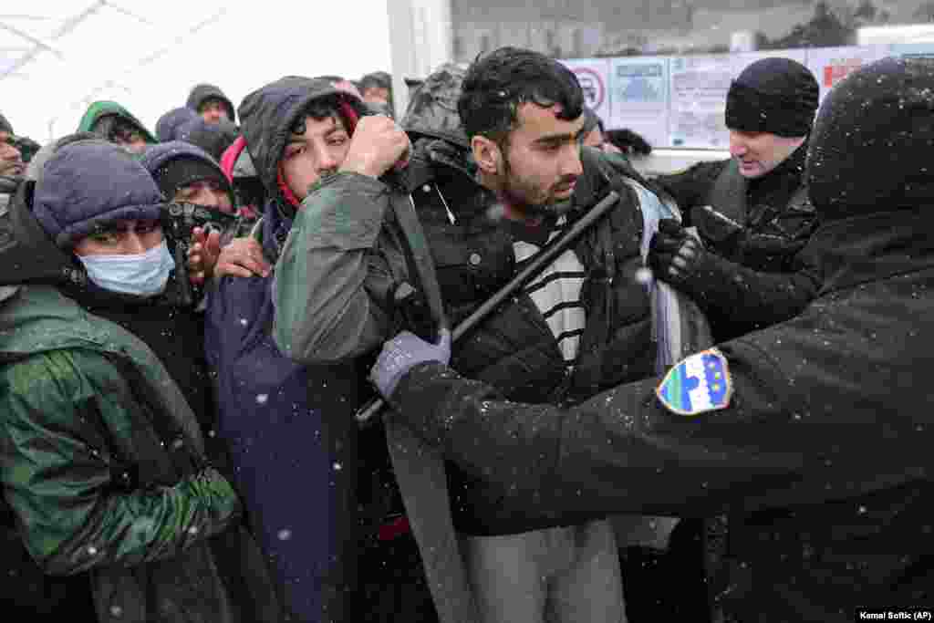 Egy rendőr menekülteket lökdös, miközben azok arra várakoznak, hogy áthelyezzék őket. A Lipa tábort december 23-án tervezték bezárni és átköltöztetni, a tűzvész azonban átírta a terveket. &nbsp;